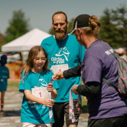 Girls on the Run 5K volunteer handing our medals at the finish line 